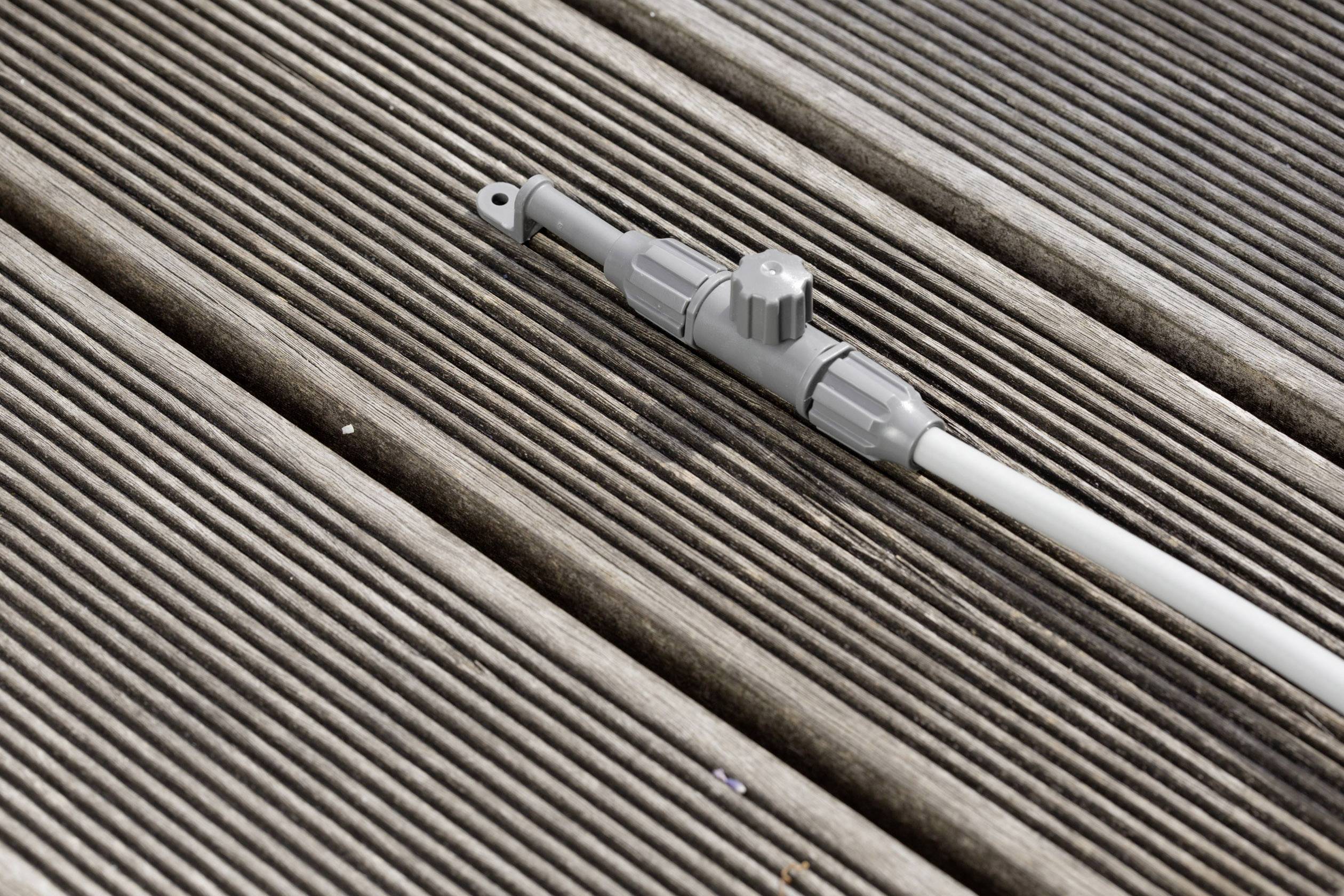 A grey garden hose connector with a twist valve is lying on a wooden decking.