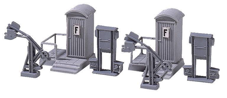 Grey model railway level crossing barriers with two small signal boxes and lever mechanisms, likely an accessory for a model railway layout.