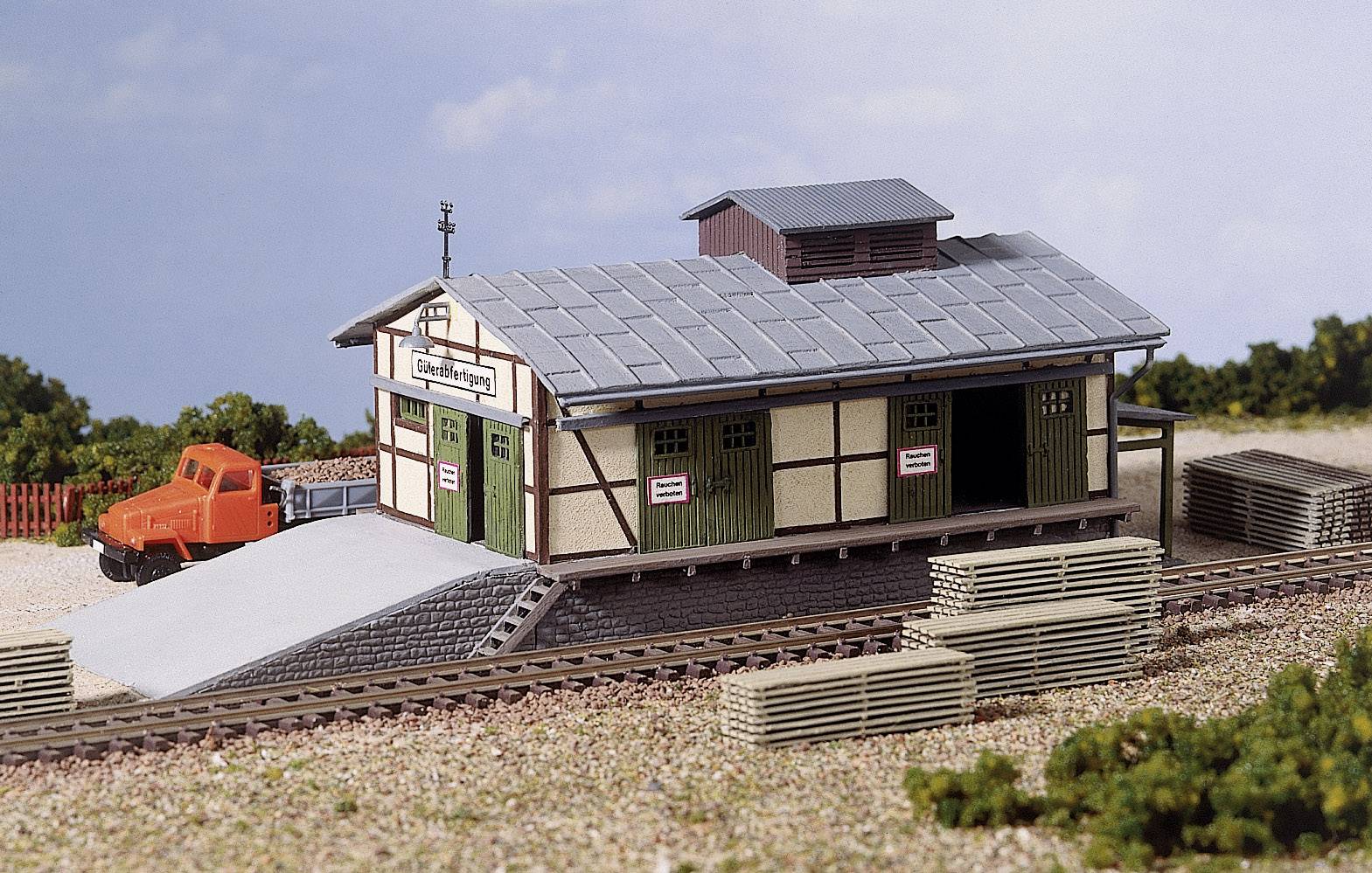 A model of a small goods yard with an orange crane vehicle beside it. Trees and blue sky are visible in the background.