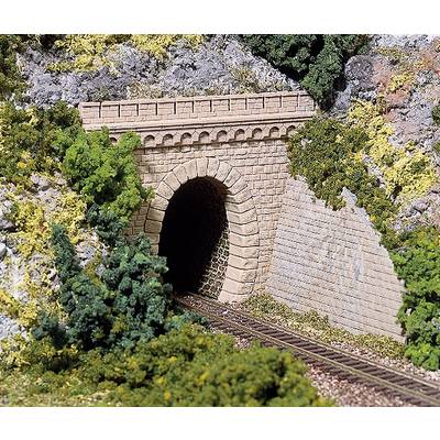 A model railway tunnel made of stone with tracks, surrounded by rocks and bushes that imitate a realistic landscape.