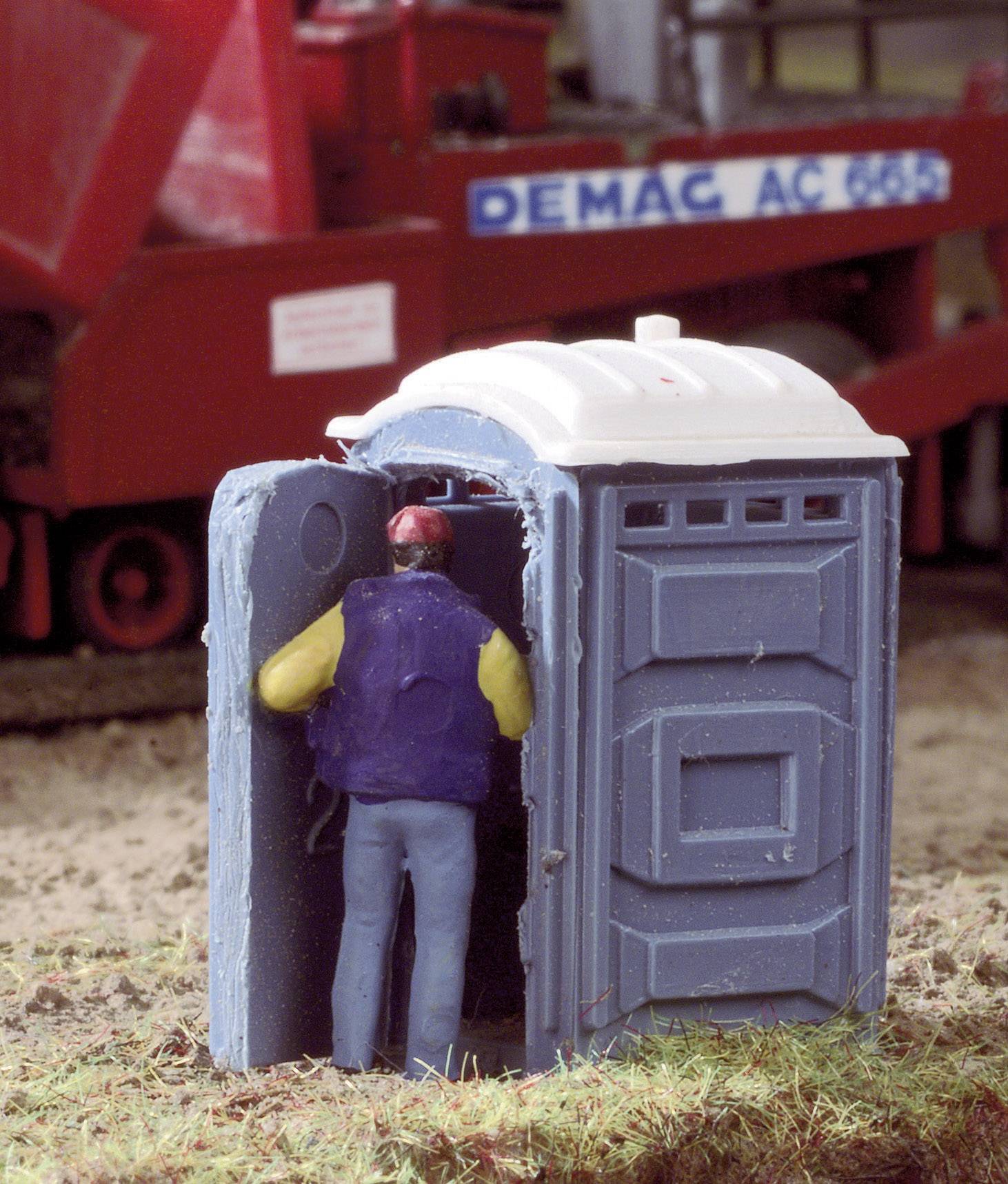 A model depicts a person entering a portable toilet. Parts of a construction vehicle are visible in the background.