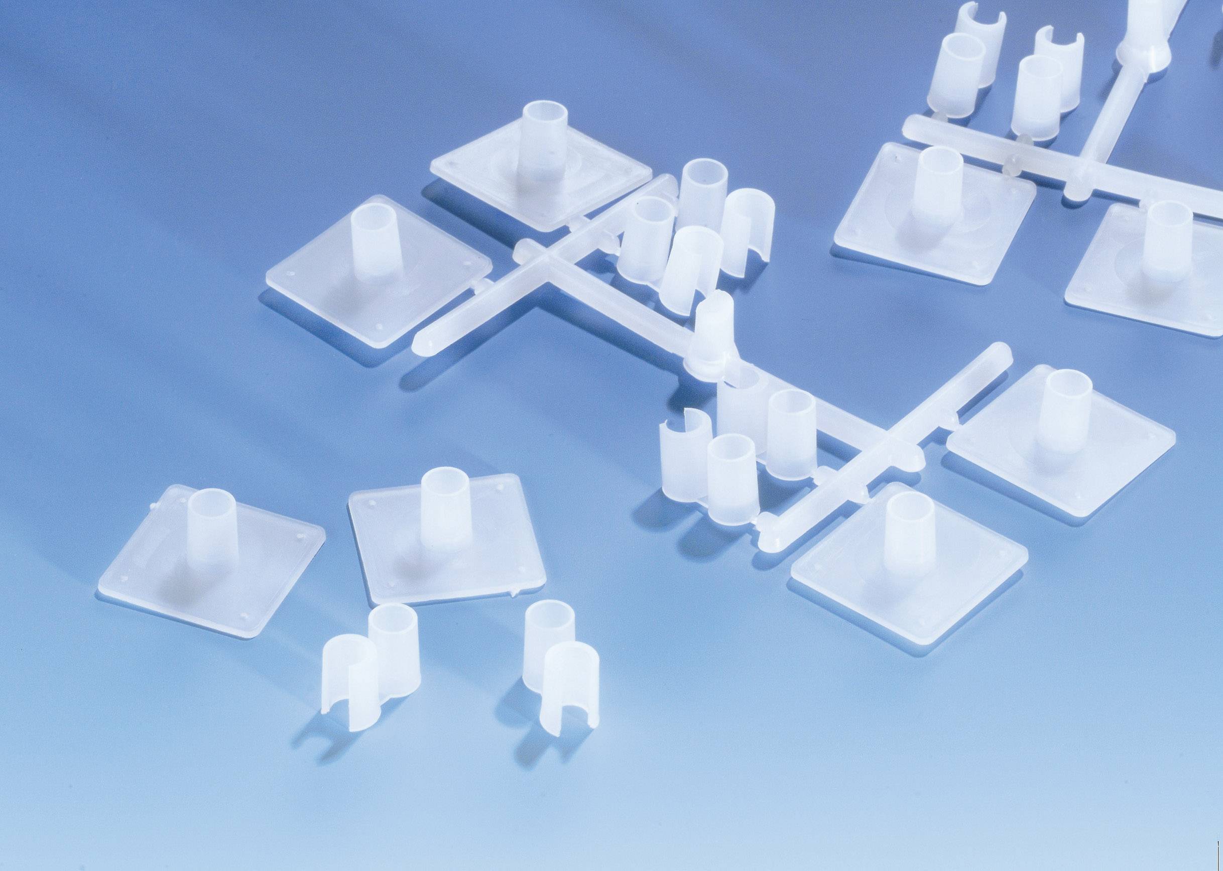 White plastic components on a light blue surface, arranged in a grid. Use for assembly or mounting purposes.