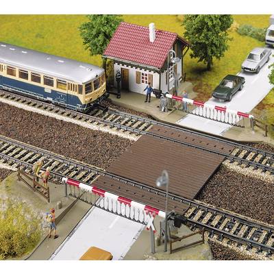 A model train passes a level crossing where people are standing and watching. Cars are waiting while the train goes by.