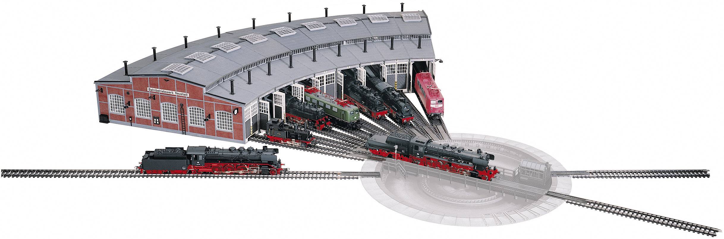 A model railway turntable with five locomotives arranged in a semicircle in front of a locomotive shed. Another locomotive is driving onto the turntable.