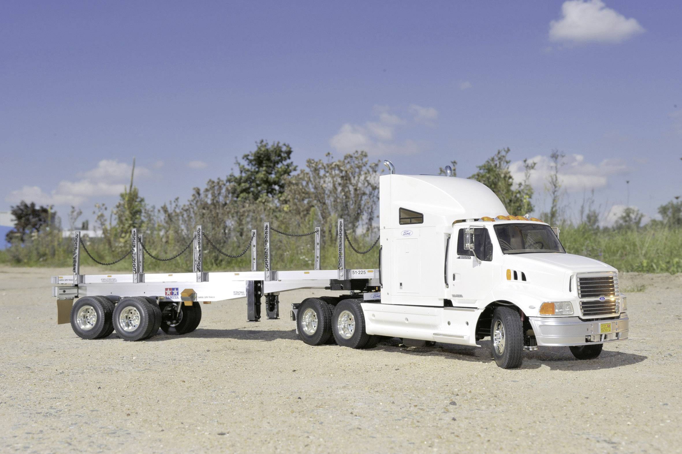 White articulated lorry with trailer on a gravel yard. The sky is blue with a few clouds. No people visible.