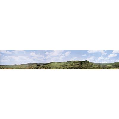 Panoramic view of a green hilly landscape under a blue sky with white clouds.