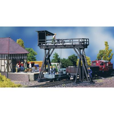 Model railway scene: Workers on and around a goods crane, a lorry being loaded. Buildings and a train are visible in the background.