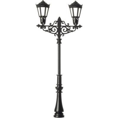 A decorative, antique metal street lamp with two lanterns, which are shining brightly. It stands against a neutral background.