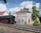 A model landscape featuring a steam locomotive beside a signal box with the inscription 'Burgstein', surrounded by trees and buildings.