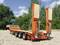 An orange heavy-duty trailer by Goldhofer is parked on a gravel area in front of a background of green trees.