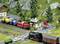 Model railway layout with a small village, tracks and two trains. A steam locomotive is pulling goods wagons, while a diesel locomotive is pulling colourful tanker cars.