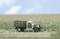 A model of a vintage lorry stands in a field. The lorry has a green and white paint finish with a wooden body. Blue sky is visible in the background.