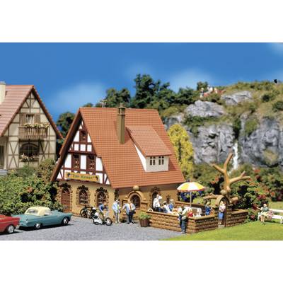A miniature village depicts half-timbered houses with red roofs, people having a picnic and bicycles. Hills and a waterfall are visible in the background.