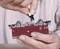 A person is holding a model train carriage and attaching a small component to its underside. Hands are securing the carriage to facilitate the attachment.