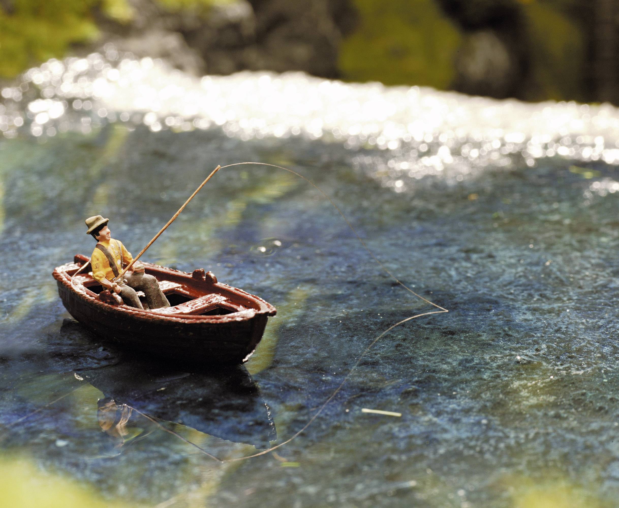 A man in a small boat is fishing on a tranquil lake. The water is clear and reflects the surrounding landscape.
