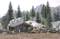 Miniature Village in Mountain Landscape: People working on a wooden cabin, surrounded by tall trees and rocks, with mountains in the background.