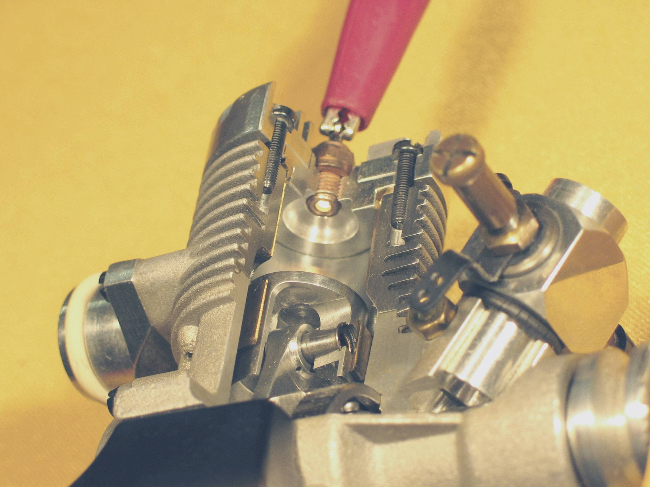 Close-up of a model aircraft engine in cross-section. Shows cylinder head, spark plug and moving parts illustrating the combustion process. Yellow background.