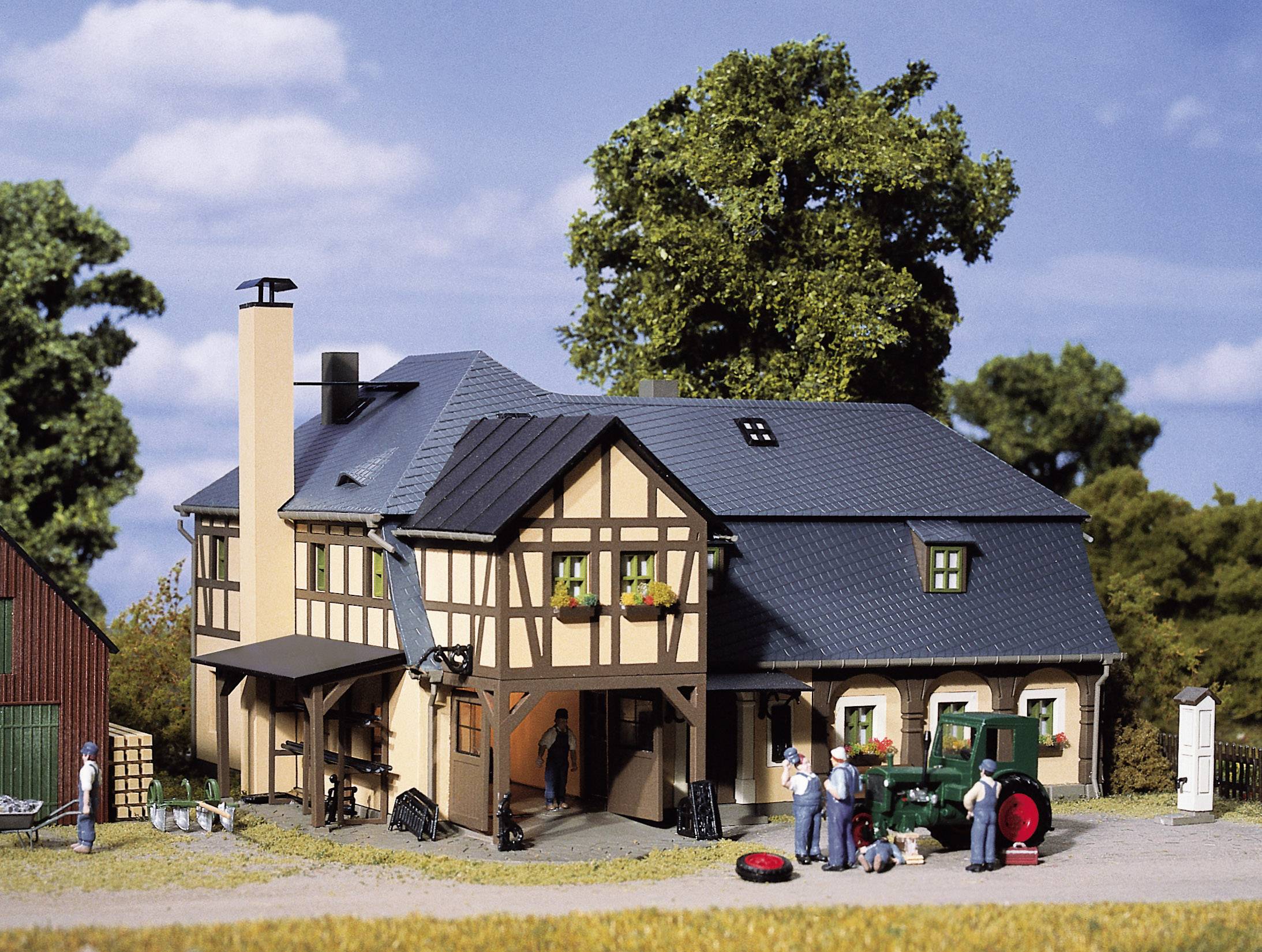 A model farmyard with a half-timbered house, surrounded by trees. In the foreground are figurines and a green tractor.