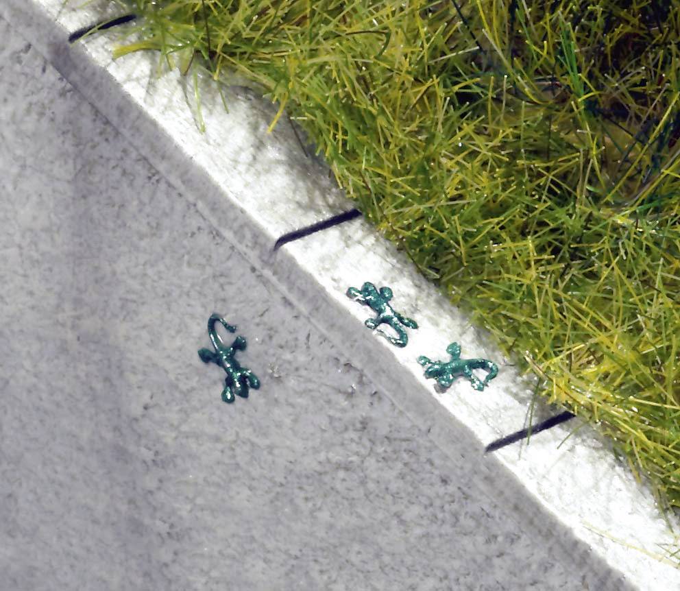 Three green heads and bodies of toads on a grey surface, near a grass-covered edge.
