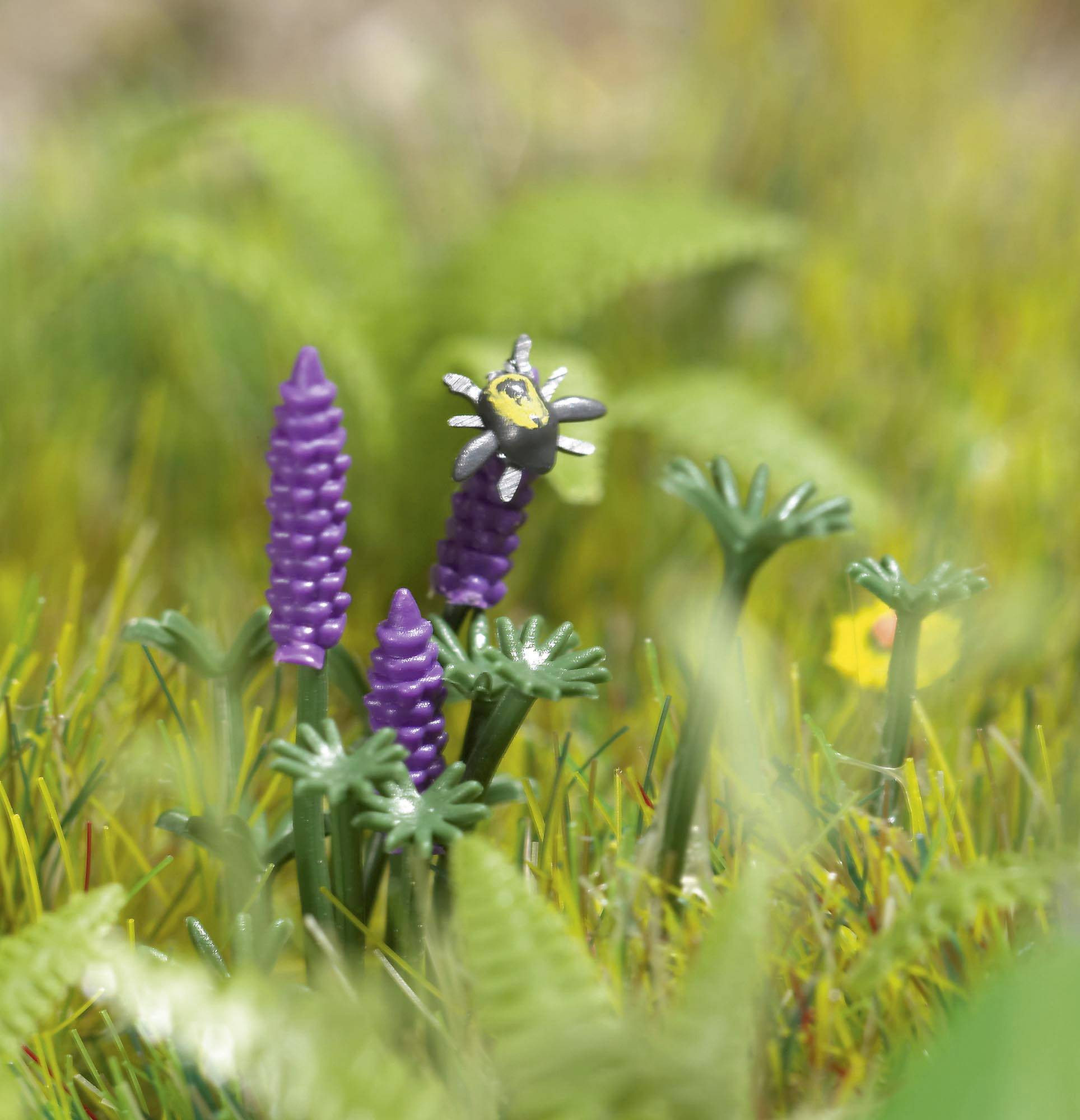 A plastic bee figurine hovers above purple blooms amid green grass.