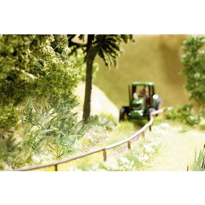 A small tractor is driving along a narrow path through a green, wooded landscape.
