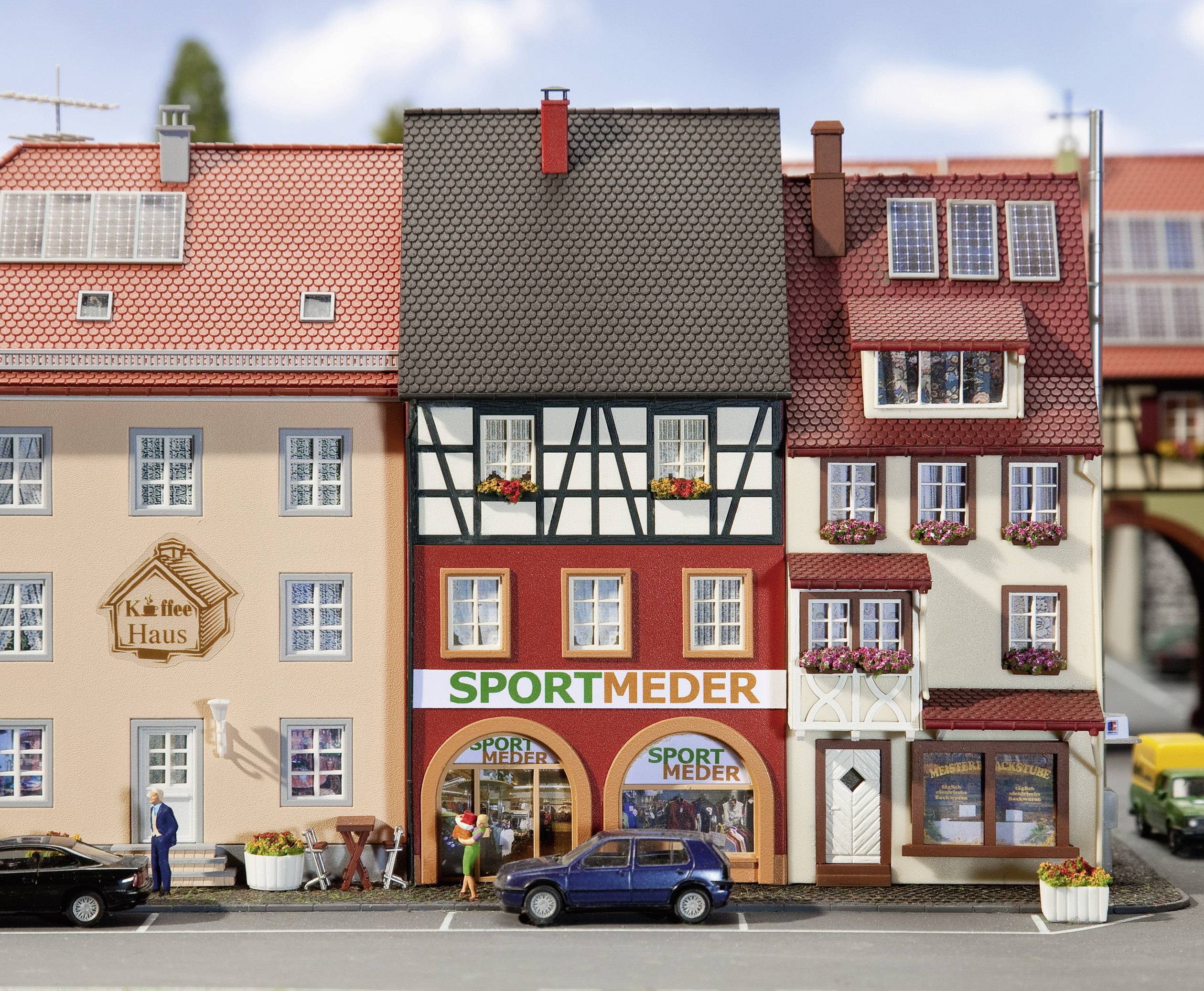Several miniature houses on a city street. Small cars are parked in front of a half-timbered house with 'Sport Meder' signage.