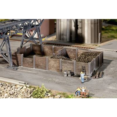 Miniature depicts a coal storage yard with wooden barriers. Two figures are seated on a bench in the foreground, while another stands near the storage area.