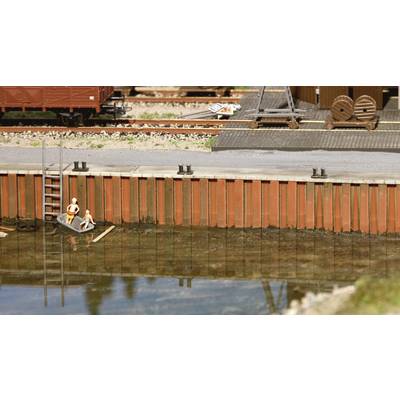 A miniature model depicts a small harbour with a boat, in which two figures are seated. In the background, railway tracks and stacks of timber can be seen.