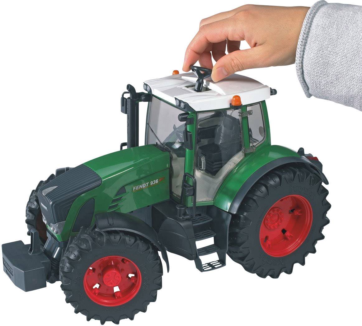 A hand operates a toy tractor in green with red wheels, simulating agricultural work.