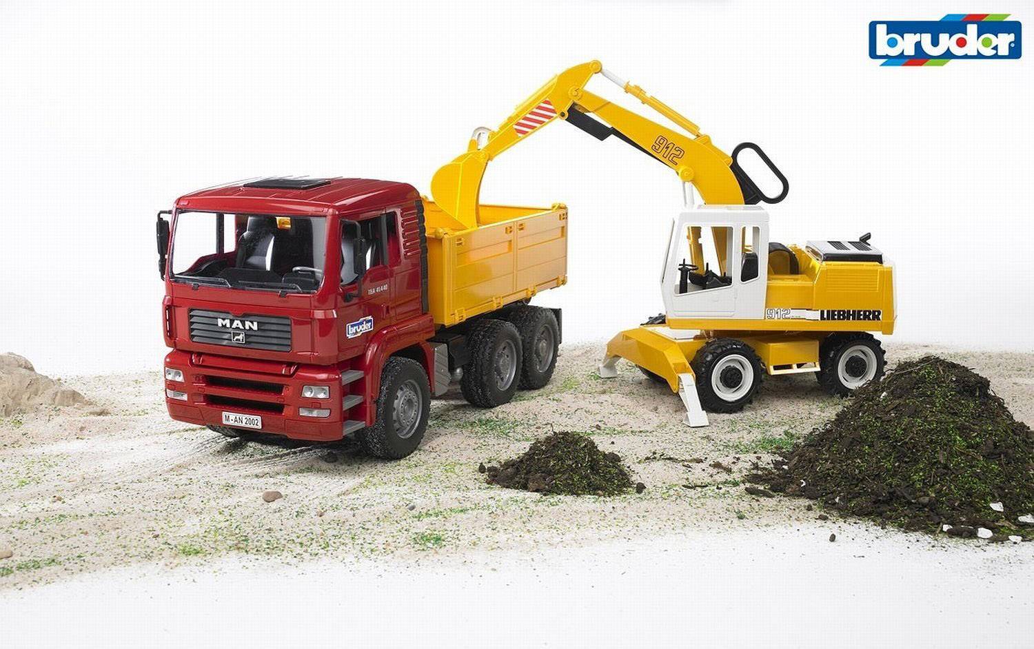 A red toy lorry and a yellow toy digger on a sandy surface. The digger is lifting earth and loading it onto the lorry.