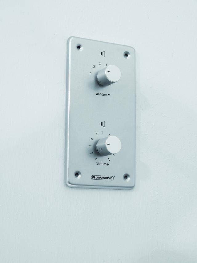 A wall panel with two rotary controls. The upper knob is labelled 'Programme', the lower one 'Volume'.