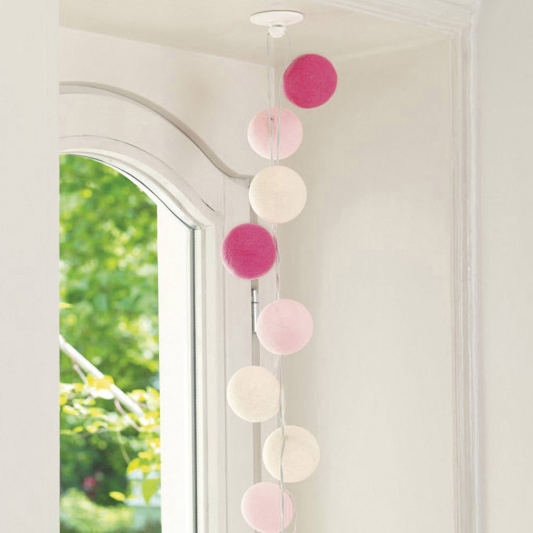 Colourful fairy lights hang on a window frame, creating a cosy atmosphere inside. A green garden is visible outside.