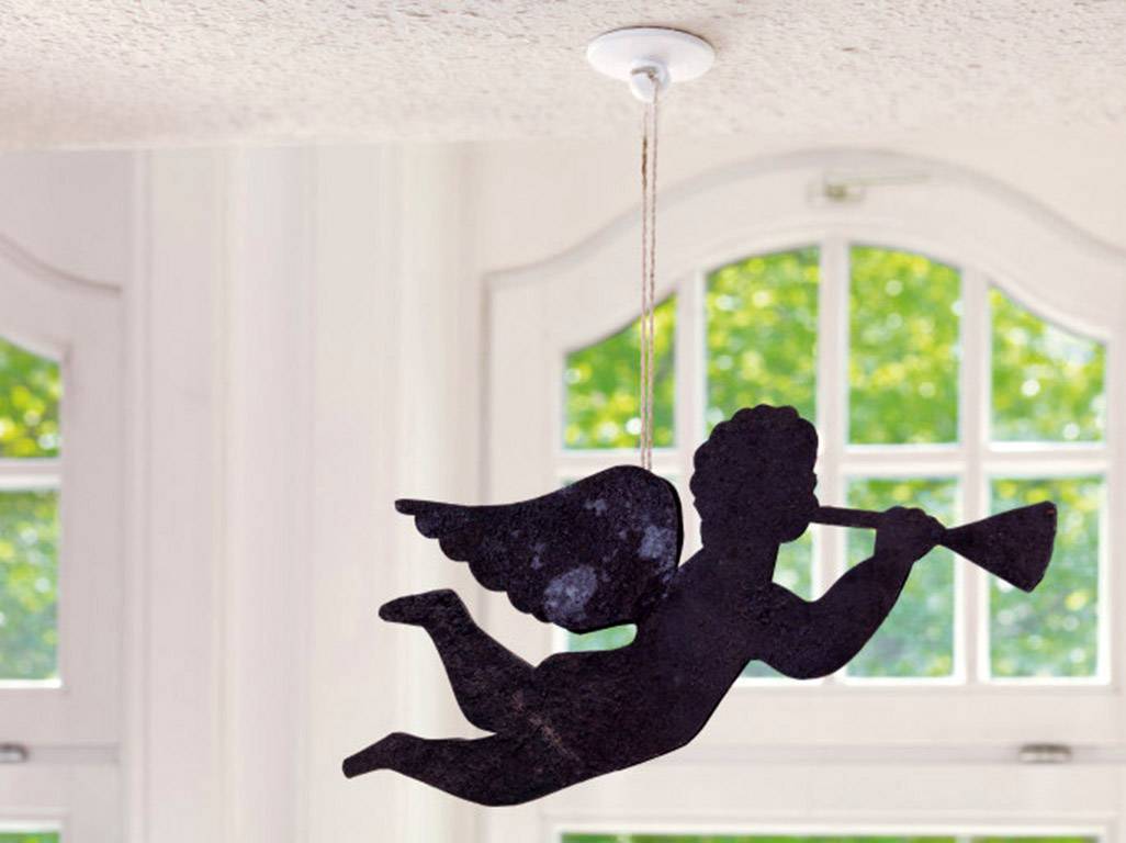 A metal angel hangs from the ceiling, playing the trumpet, in front of a window overlooking green trees.