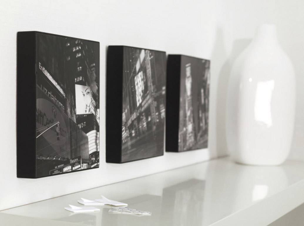 Three black and white photographs of urban scenes side by side on a shelf, with a white vase beside them.