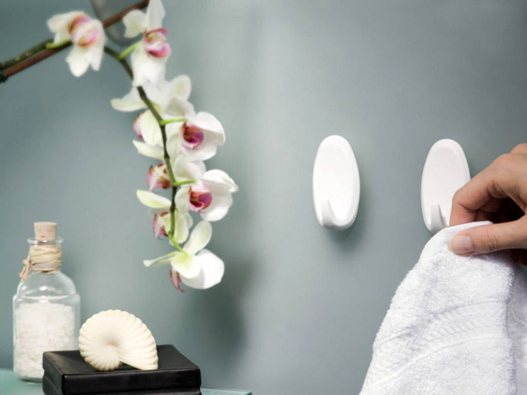 A hand hangs a towel on a white hook. Next to it, an orchid, a glass of bath salts, and a seashell.