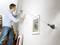 A man is mounting a picture on a wall using a laser tool attached to the wall to ensure straight alignment.