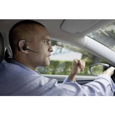A man is driving a car and wearing a headset, looking focused. The journey appears to be taking place during daylight.