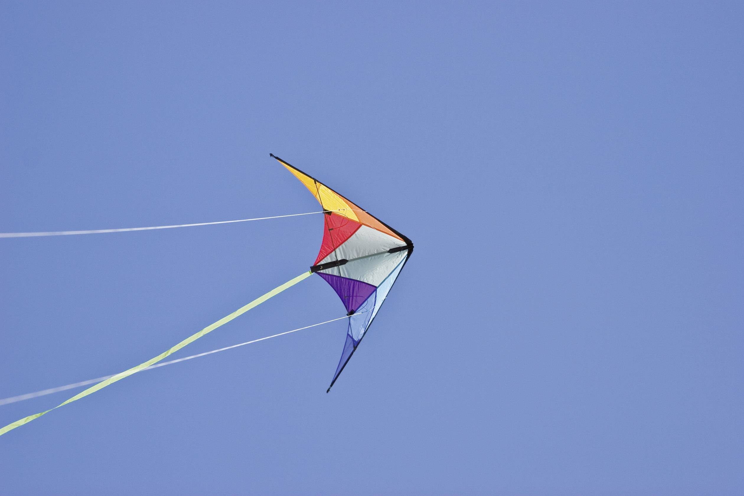 A colourful kite with a triangular shape flies in the blue sky, its strings fluttering in the wind.