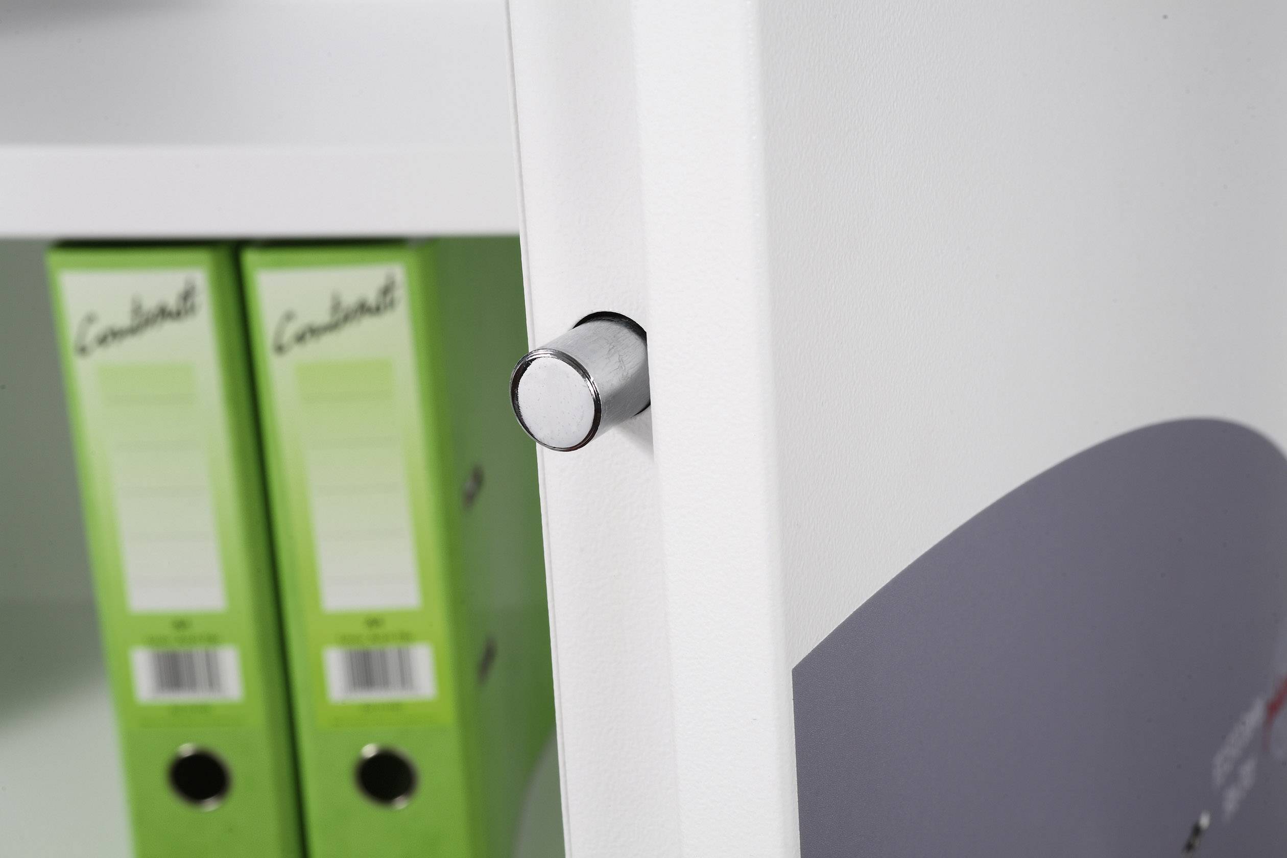 A silver button on a white door in the foreground, with two green folders on a shelf behind it.