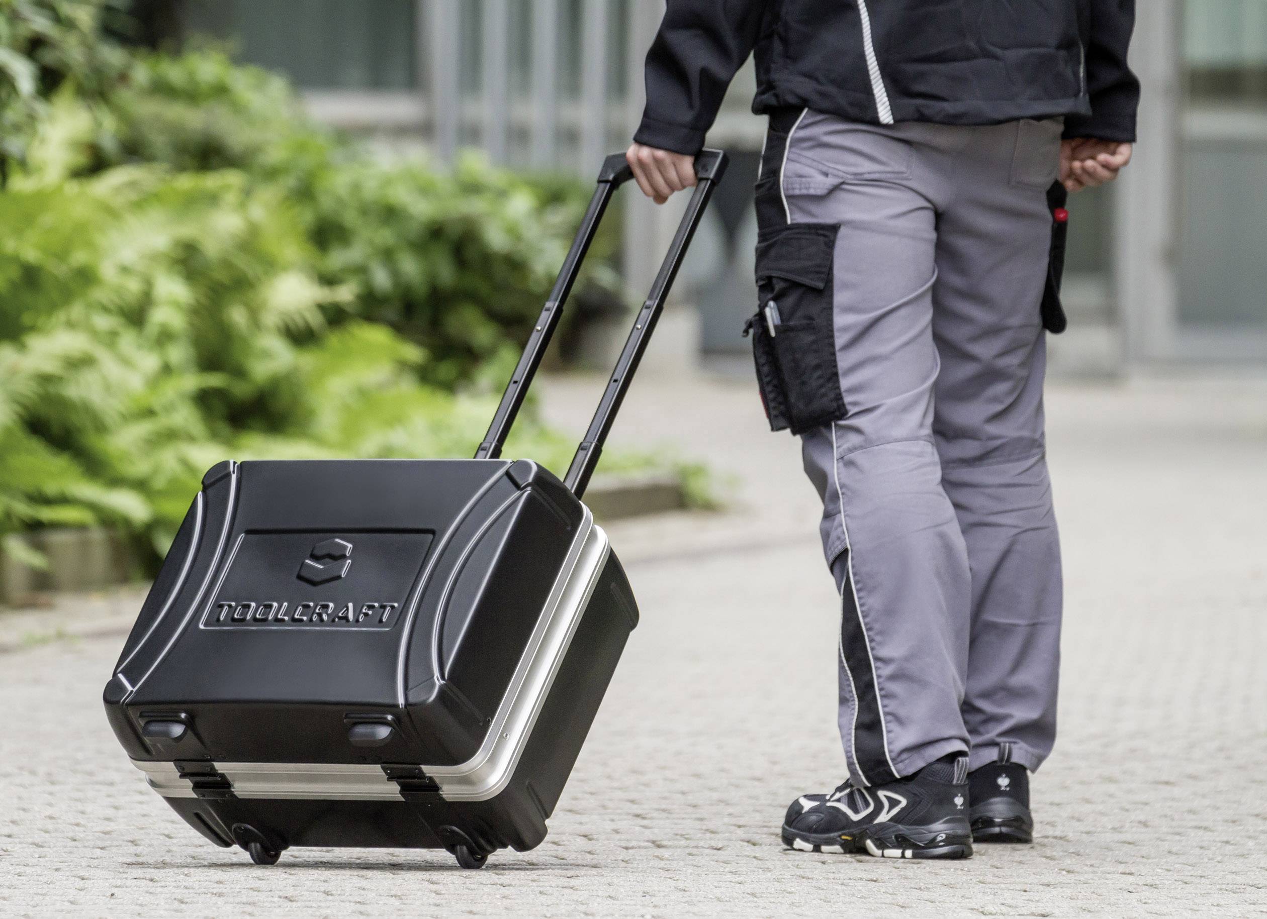 A person is pulling a black tool case with an extendable handle across a paved path.