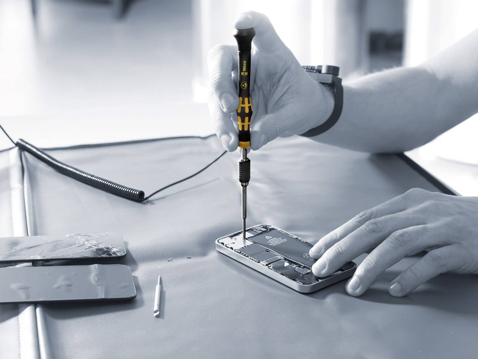 A person is repairing a smartphone by working on the internal components with a screwdriver.