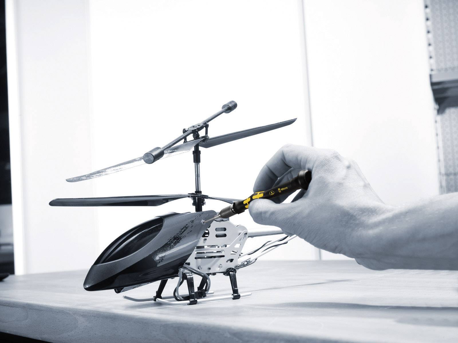 A hand is repairing a small helicopter with a screwdriver on a table.