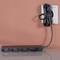 A blank, black power strip is lying on a table. A power cable is neatly coiled and plugged into a wall socket.