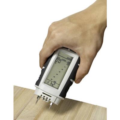 A hand holds a digital moisture metre against a wooden board. The device displays measurement readings on its screen.