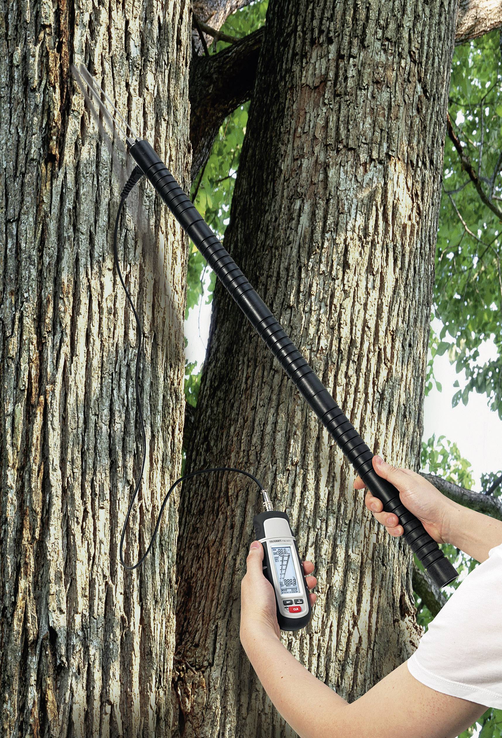 A person is measuring the moisture of a tree trunk using an electronic measuring device attached to a long pole.
