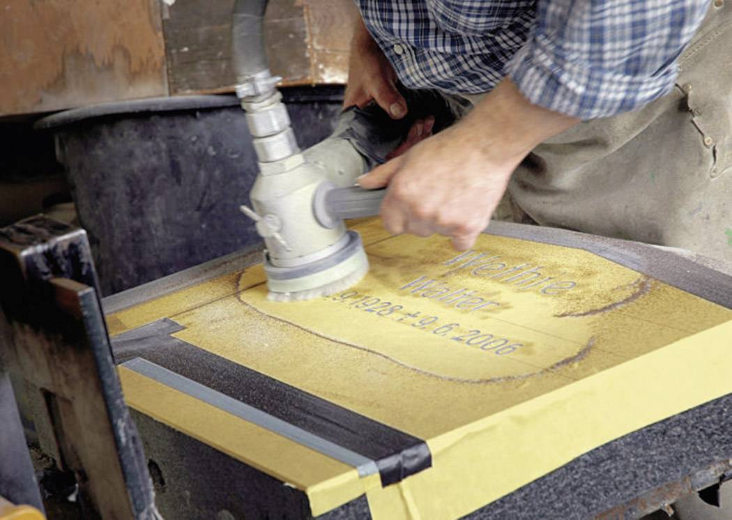 A person is grinding a headstone with a machine. The headstone displays the name 'Werther' and the years 1953-2006.