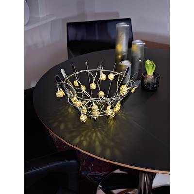A round table with decorative lights in a basket in the centre, accompanied by candles and a small green plant.