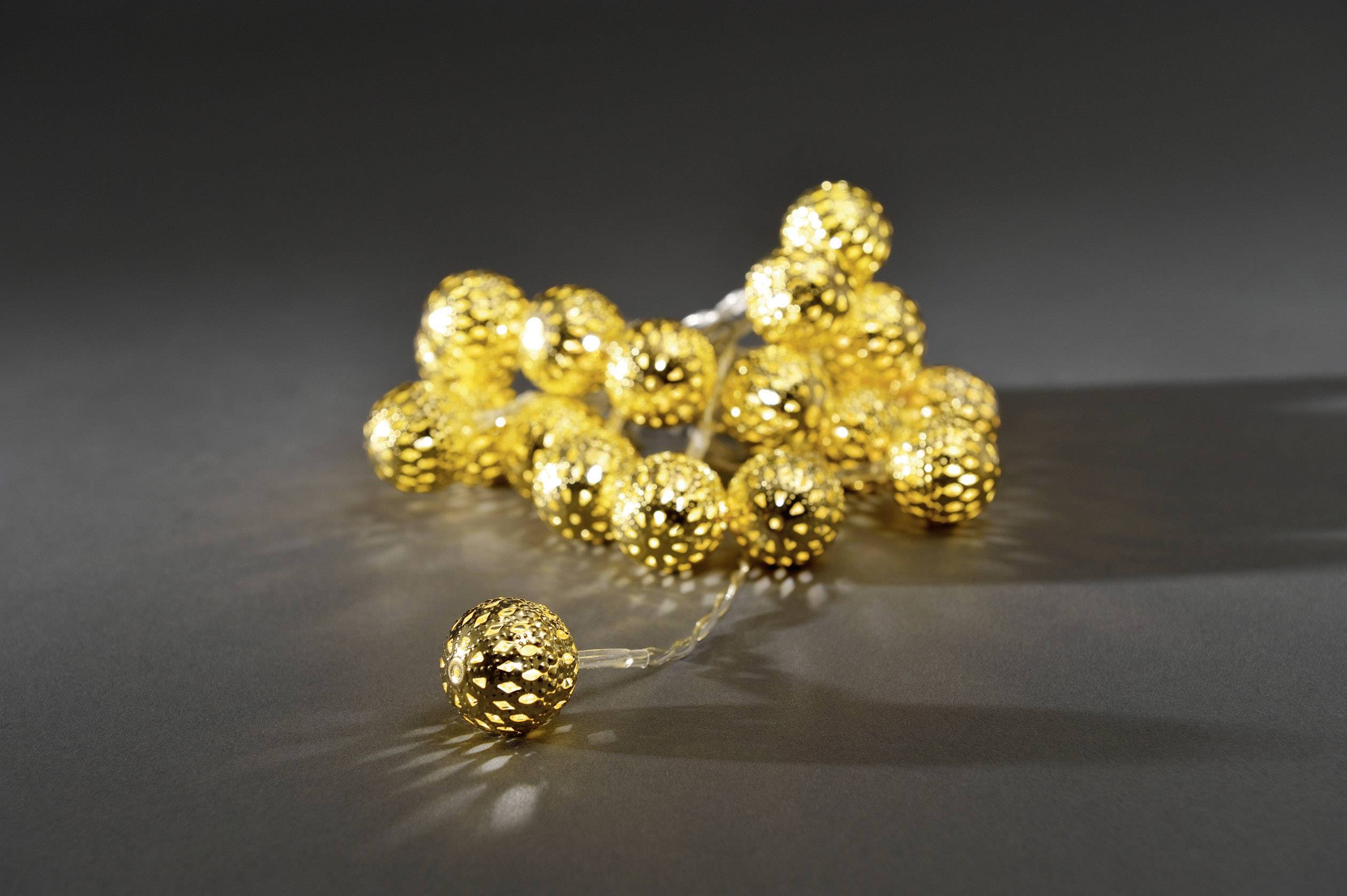 A string of fairy lights with gold-coloured baubles rests on a dark surface, radiating a warm glow and creating atmospheric lighting.