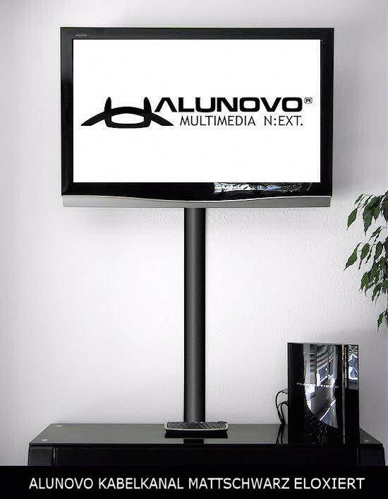 A flat screen mounted on a black cable trunking with the 'Alunovo Multimedia N:EXT' logo. Beneath it, a cabinet with equipment.