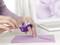 A person is using a hand-held tape dispenser to seal a purple envelope. A laptop is visible in the background.